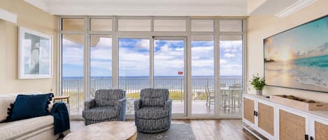 A spacious living room with a large sliding glass door leading to a balcony with a view of the ocean.