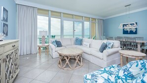 A spacious living room with a white sofa, round coffee table, and a view of the sea through large windows.