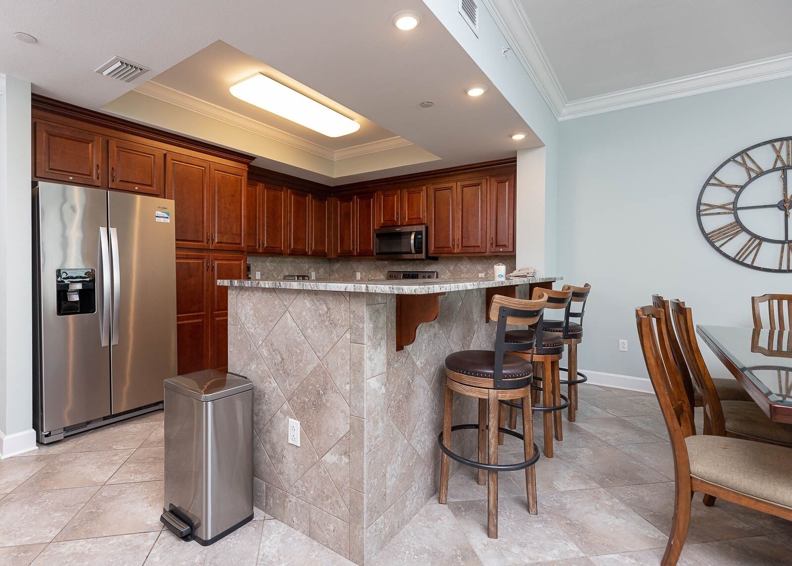 A modern kitchen with a stainless steel refrigerator, a microwave, and a marble island with bar stools.