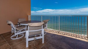 A balcony with a view of the ocean, a round table, and two chairs with cushions. - Phoenix Orange Beach 1204 3 Bedroom Condo (Orange Beach)