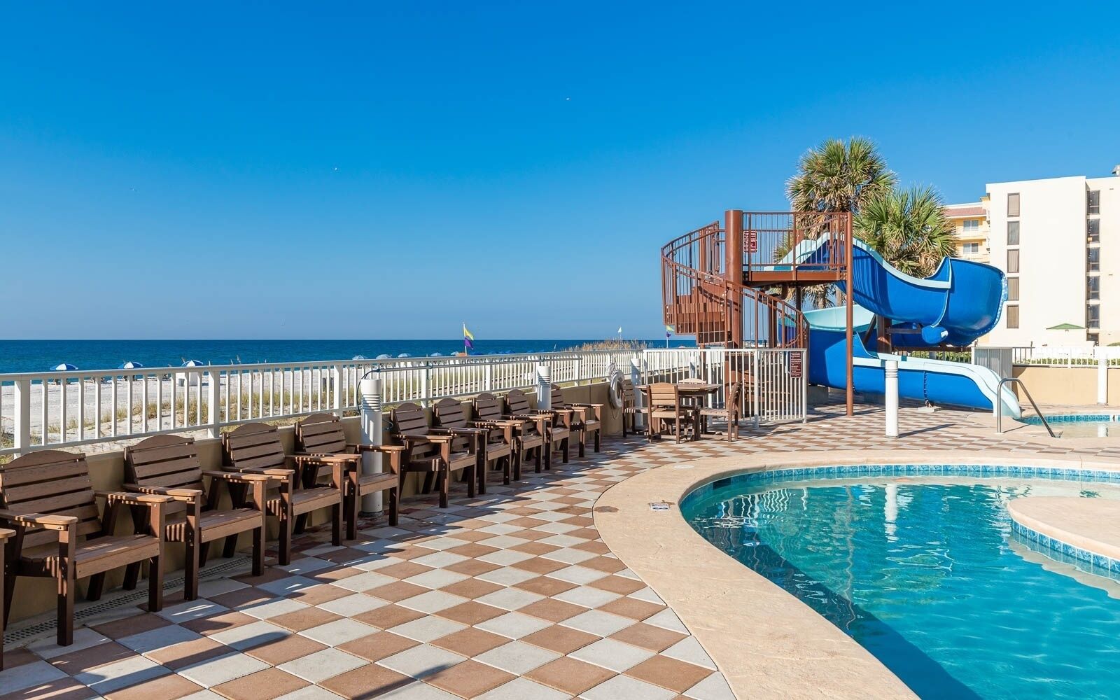 A poolside area with a checkered floor, lounge chairs, and a blue water slide.