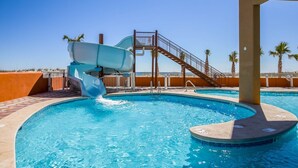 En swimmingpool med en vattenrutschkana, en trappa och palmer i bakgrunden.