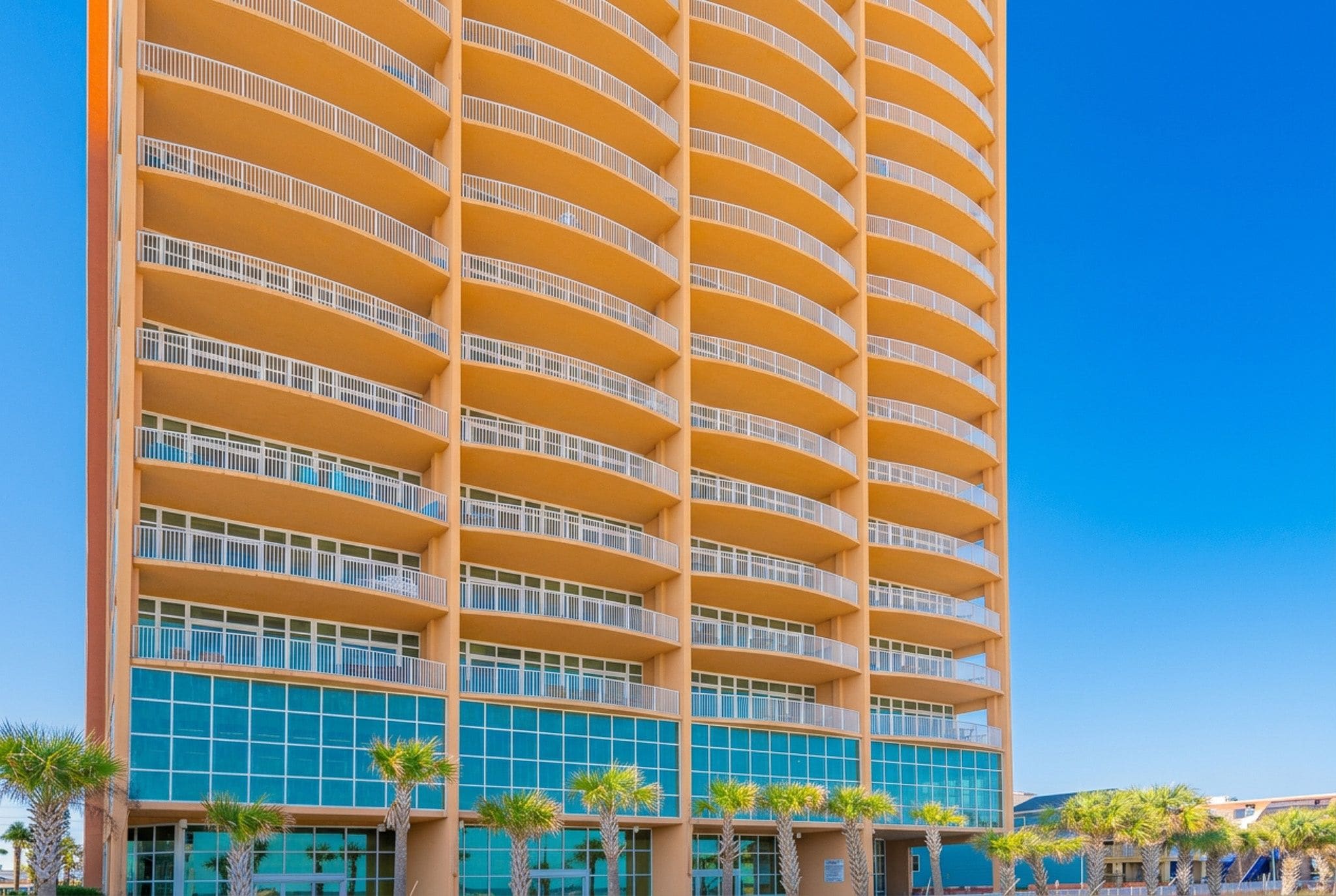 Un hotel de varios pisos con balcones, fachada azul y palmeras al frente.