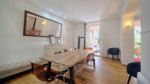 Een moderne eetruimte met een houten tafel, transparante stoelen, een gestoffeerde bank en een grote spiegel aan de muur.