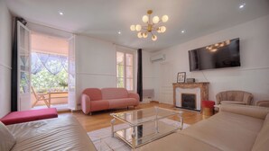 Een moderne woonkamer met een glazen salontafel, een bank, een roze fauteuil en een open haard.