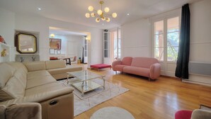 Een ruime woonkamer met een beige bank, een roze fauteuil en een glazen salontafel.