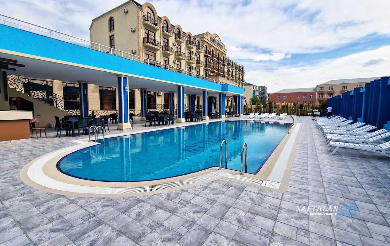 Ein Swimmingpool mit Liegestühlen und einem überdachten Sitzbereich, umgeben von einem Gebäude mit mehreren Balkonen.