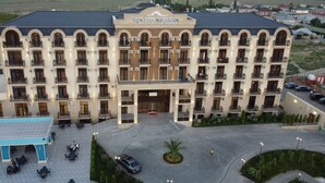 Un hotel de varios pisos con entrada central, balcones y un estacionamiento.