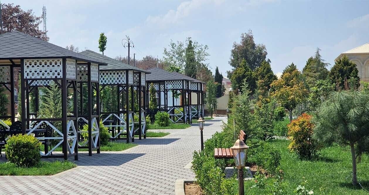 A pathway lined with wooden gazebos and a lamp post, surrounded by greenery and trees.
