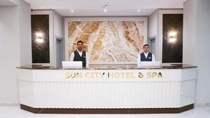 Una recepción en el Hotel & Spa Sun City con un fondo de pared de mármol y dos empleados detrás.