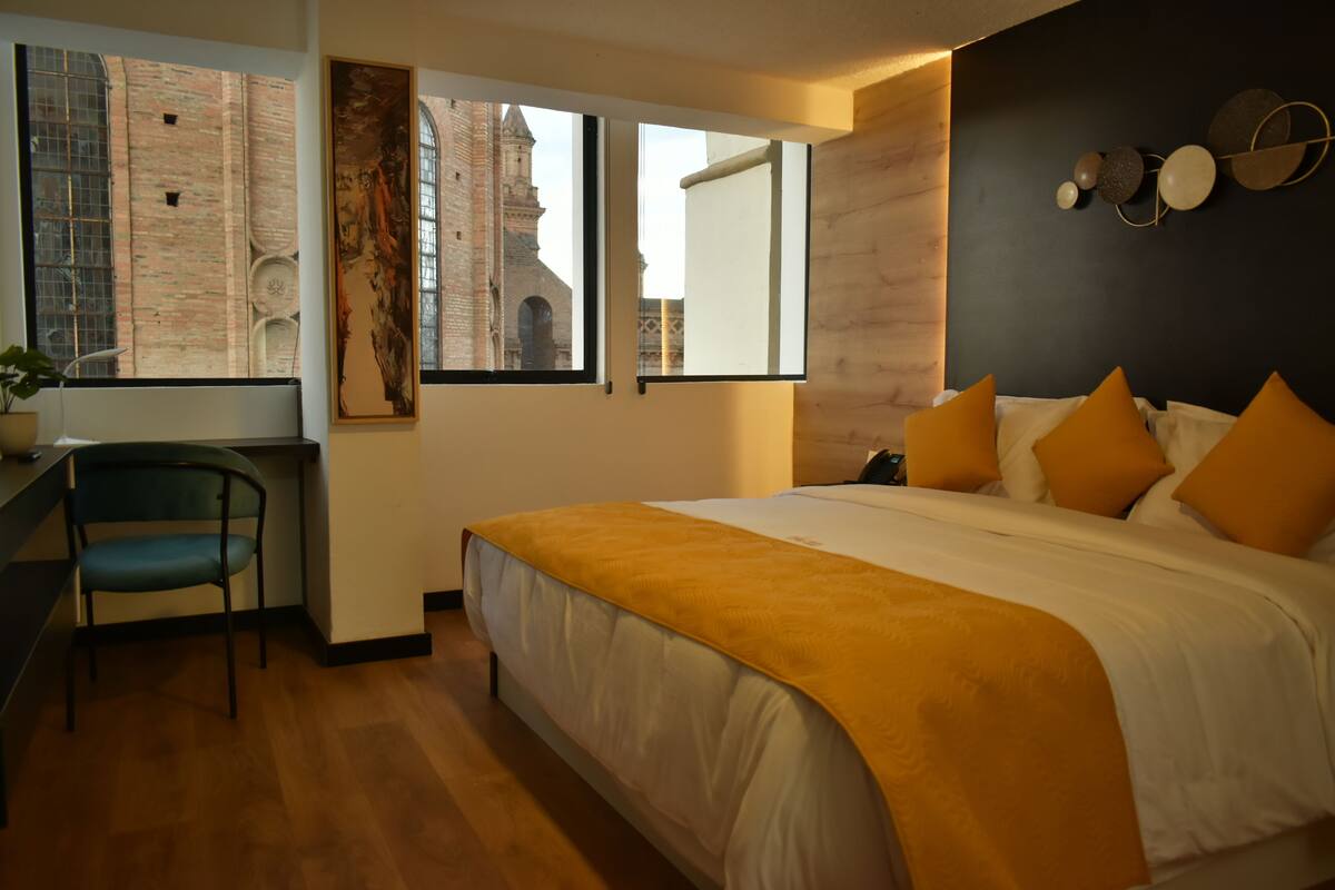 Habitación de hotel moderna con una cama grande, un escritorio y vistas a un edificio histórico a través de amplios ventanales.