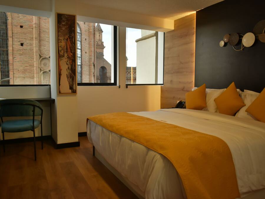 Ein modernes Hotelzimmer mit einem großen Bett, einem Schreibtisch und Blick auf ein historisches Gebäude durch große Fenster.