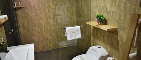 Un baño con cabina de ducha de vidrio, inodoro blanco y lavamanos.
