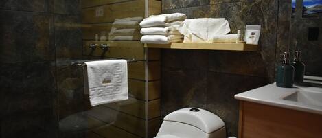 A modern bathroom with a white toilet, a glass shower enclosure, and a wooden shelf with folded towels.