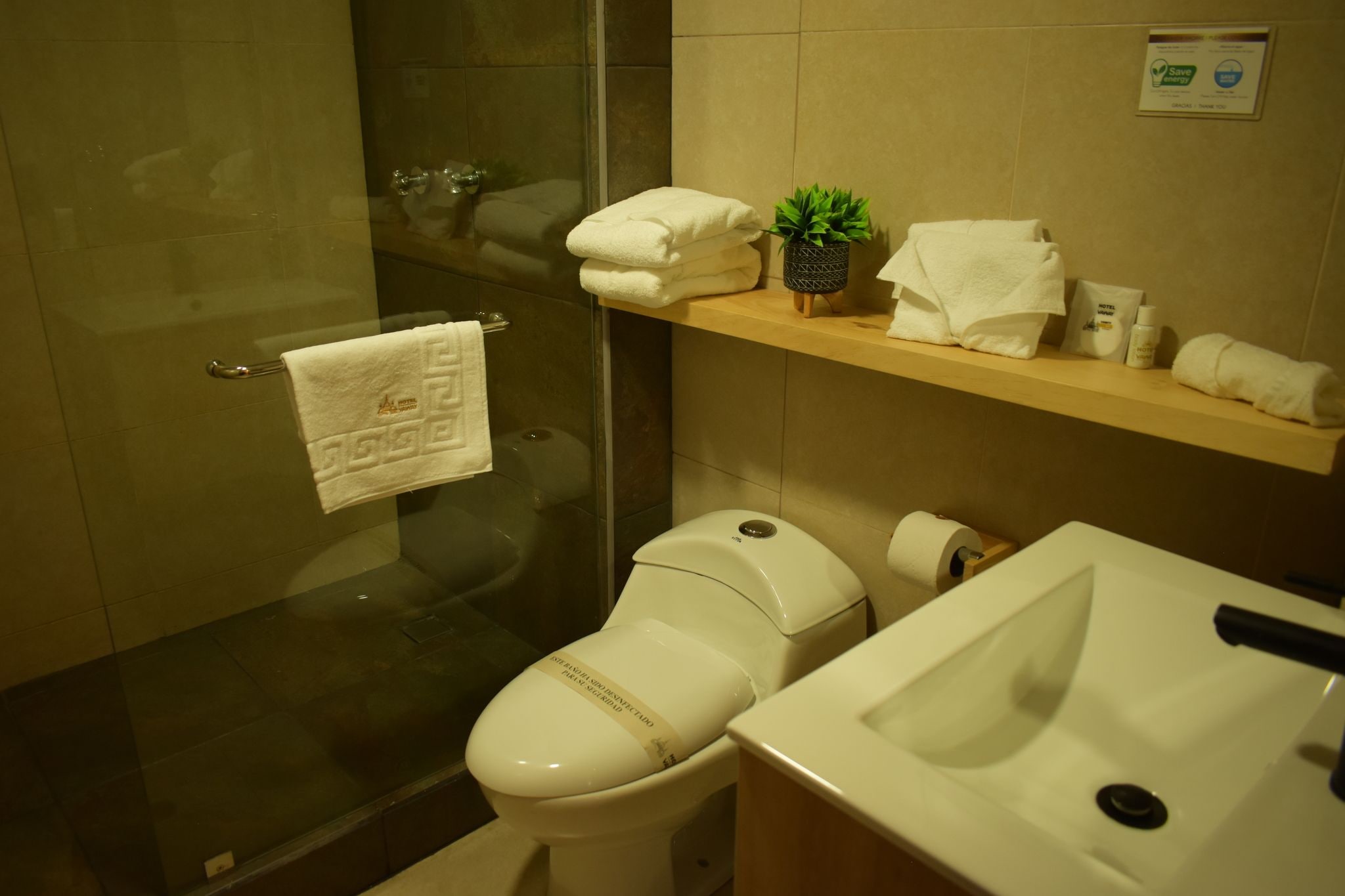 A bathroom with a glass shower enclosure, a toilet, a sink, and a towel rack with towels.