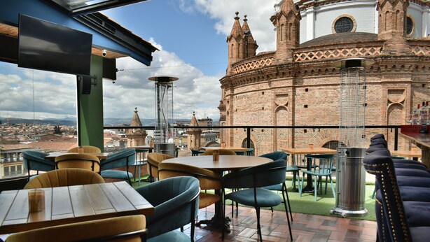 Un patio exterior con mesas y sillas, un cubo de basura y vistas a un edificio histórico con cúpula y torres.