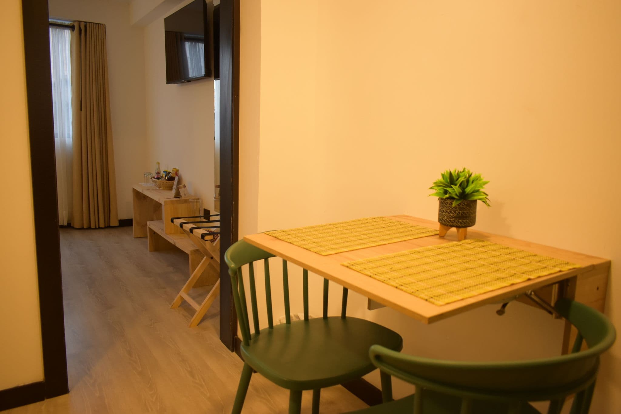 Una habitación pequeña con una mesa, sillas, una planta y un televisor instalado en la pared.