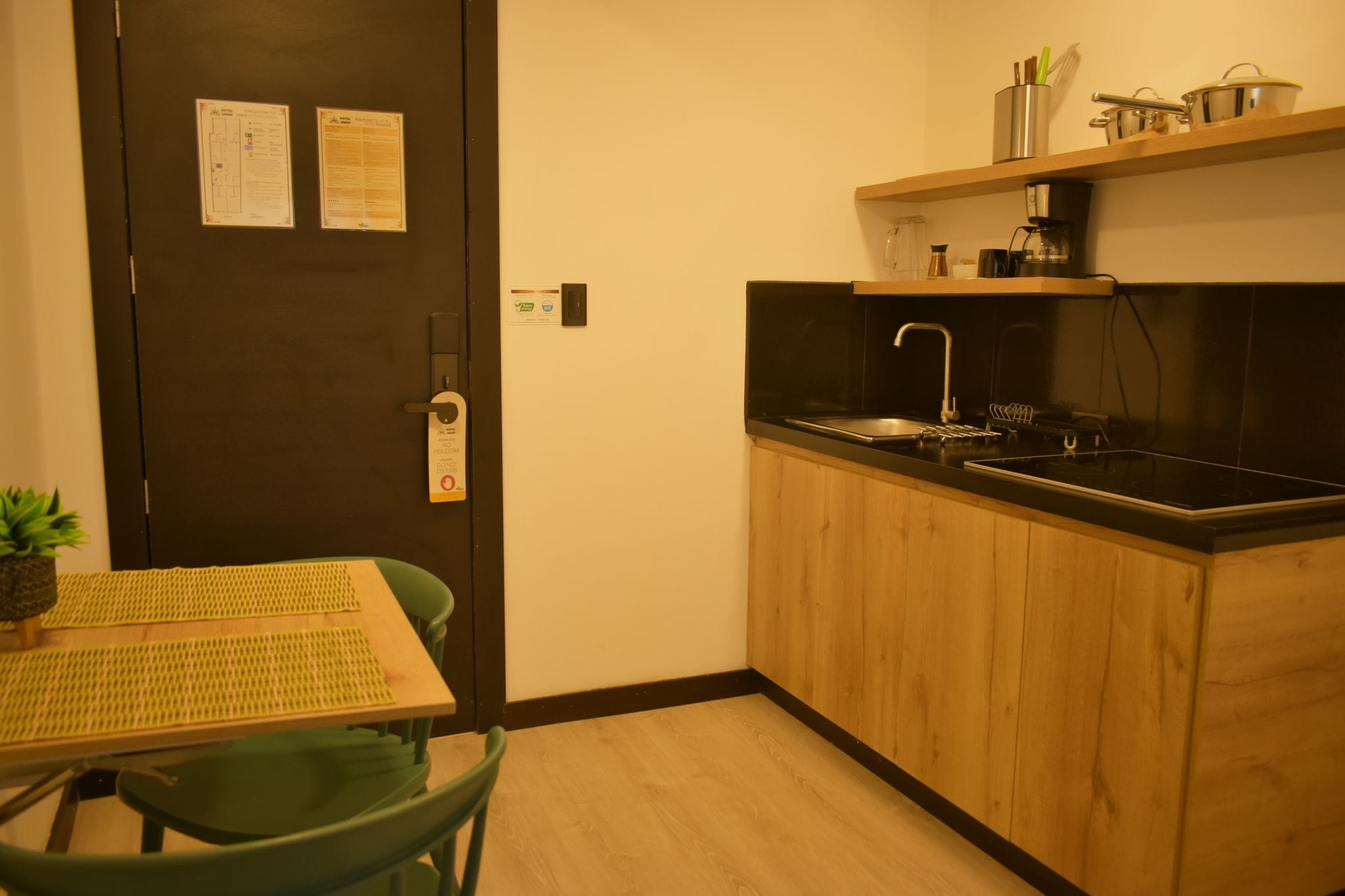 Une petite cuisine équipée d’un évier, d’une cuisinière et d’un petit plan de travail. On y trouve une table en bois avec des chaises et une plante en pot.