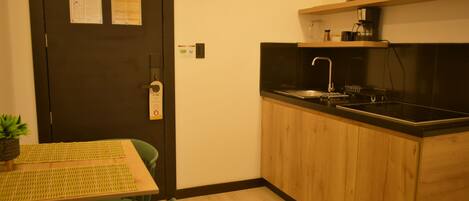 A compact kitchen with a sink, a stove, and a small countertop. There is a wooden table with chairs and a potted plant.