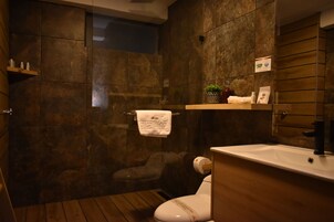 Un baño con suelo de madera, inodoro blanco, lavabo con espejo y zona de ducha.