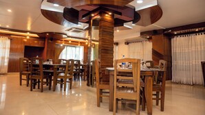 Uma sala de jantar espaçosa com mesas e cadeiras de madeira, uma coluna central e um design moderno no teto.
