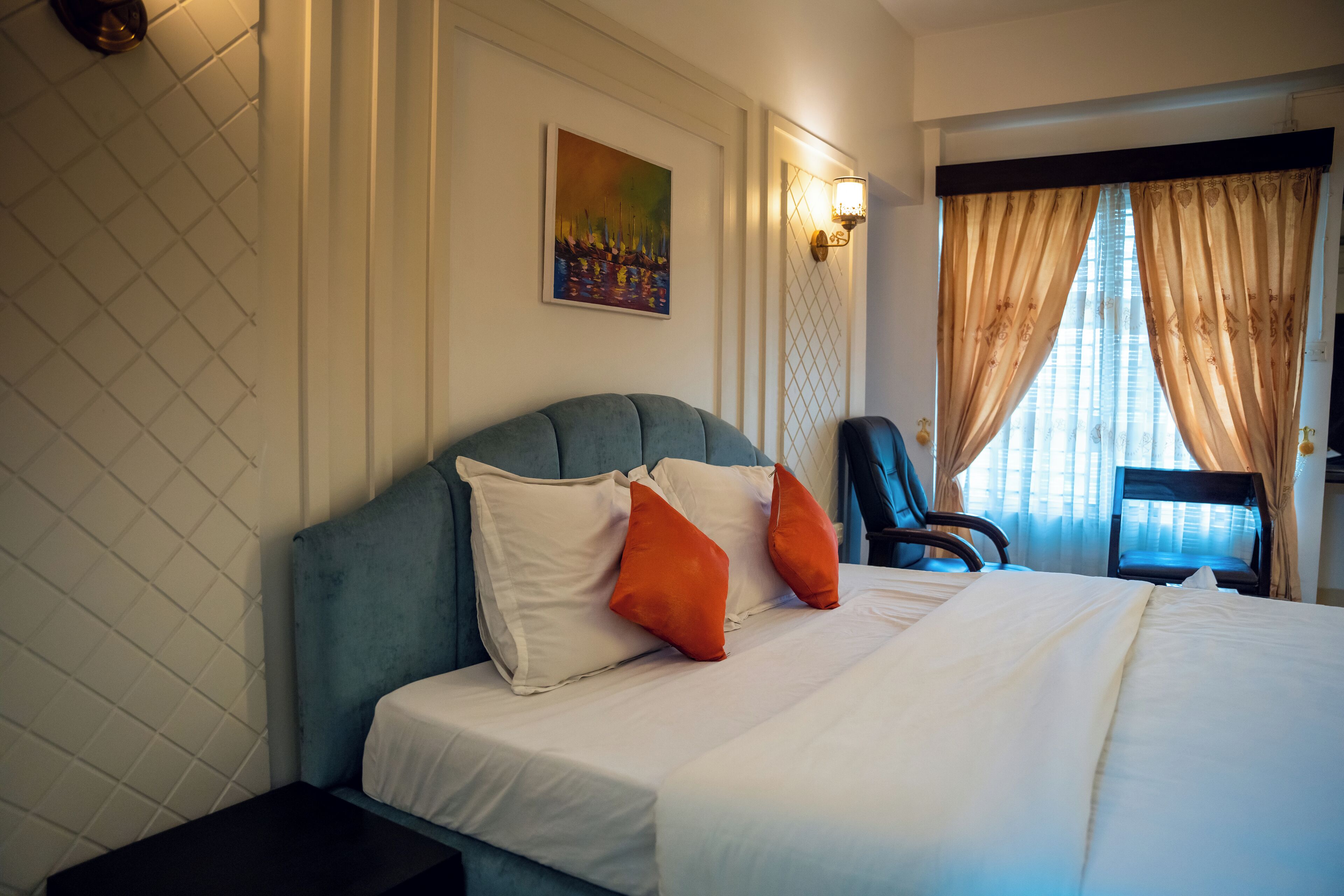 Una habitación de hotel con cama, una silla, un cuadro en la pared y un ventanal con cortinas.