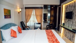Quarto de hotel com uma cama grande, uma escrivaninha, uma cadeira, uma televisão e um quadro na parede.