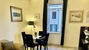 Een woonkamer met een bank, een eettafel met stoelen, een tv-meubel en een raam met gordijnen.