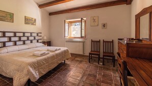 Une chambre à coucher avec une tête de lit en bois, un grand lit recouvert d’une courtepointe, une commode en bois, une fenêtre donnant sur un beau paysage et un radiateur.