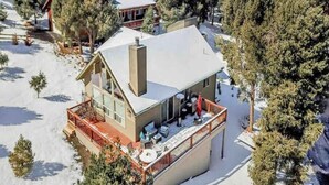 Une maison recouverte de neige, dotée d’un balcon et d’une terrasse, entourée d’arbres.