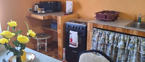 A compact kitchen with a stove, microwave, and a small refrigerator. A dining table with yellow flowers and a vase is set with plates and cutlery.