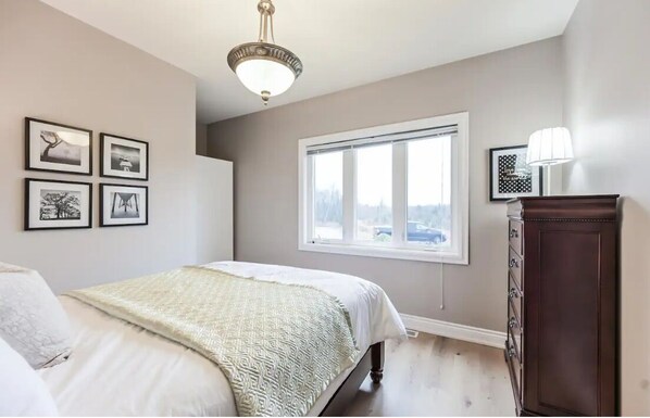 Een slaapkamer met een bed, een dressoir, een raam en wanddecoratie.