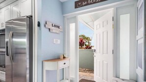 Una cocina moderna con un refrigerador de acero inoxidable, una mesita blanca y una puerta que da a un balcón con plantas.
