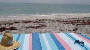 Una playa con una manta a rayas y un sombrero de paja.