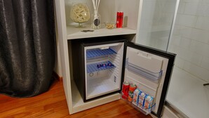 A compact refrigerator with a freezer compartment, a shelf with decorative items, and a small shelf with beverages. - Navona Vita Suites (Rome)