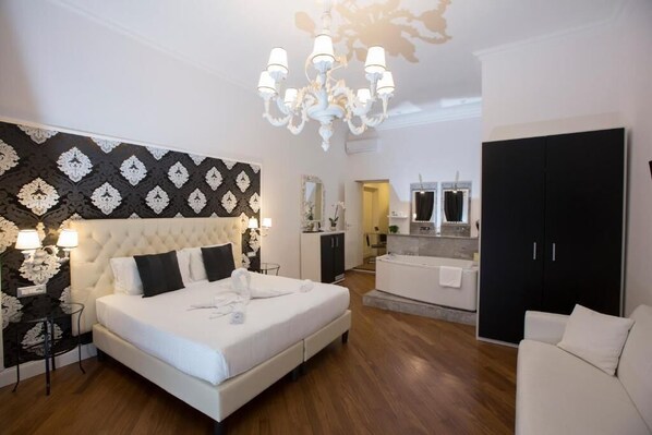 A bedroom with a large bed, a chandelier, a wardrobe, and a bathroom in the background.
