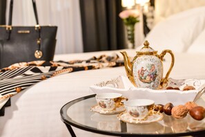 Une table avec une théière, des tasses et des biscuits disposés sur un plateau, le tout posé sur un lit recouvert d’une couvre-lit à motifs, avec un sac à rayures noires et blanches en arrière-plan.