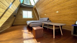 Um quarto de sótão aconchegante, com paredes de madeira, uma cama beliche, uma mesinha e um banco.