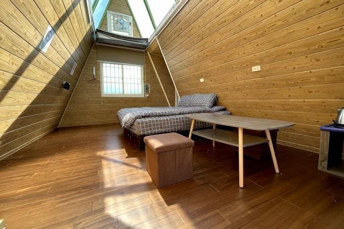 A small, wooden-paneled attic room with a bed, a table, and a bench.