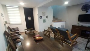 Zona de menjador amb taula i cadires de fusta, un bol decoratiu petit, i una escala que mena a un pis superior.