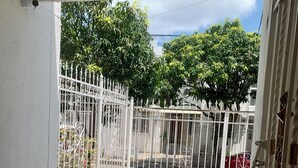 Un balcó tancat amb barana, un paviment de rajoles, una paret blanca i vista d'un carrer amb arbres i cotxes estacionats.