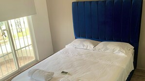 Un llit ben fet amb llençols blancs i dues tovalloles enrotllades, un reposacapses blau i un sòl de fusta.