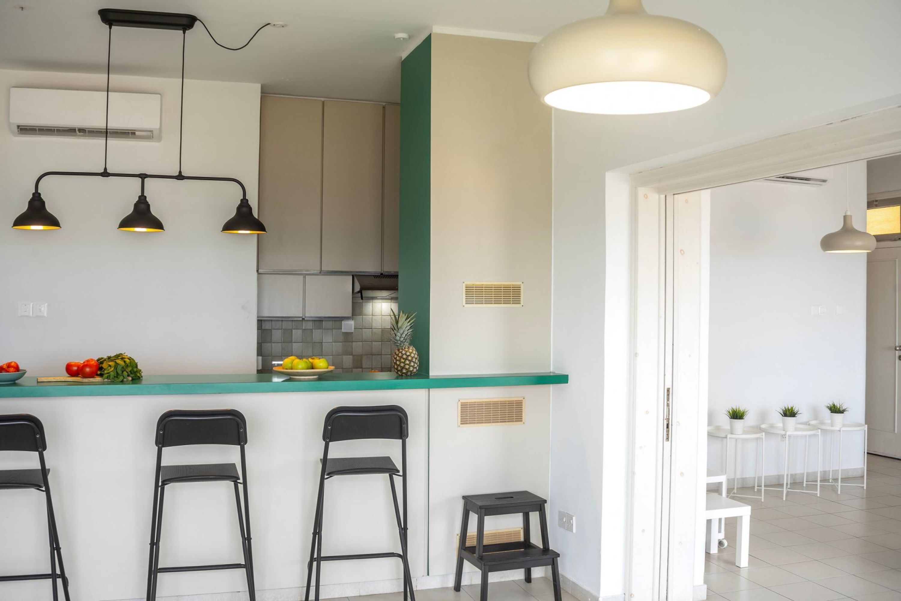 A modern kitchen with a green countertop, three black pendant lights, and a white ceiling fan.