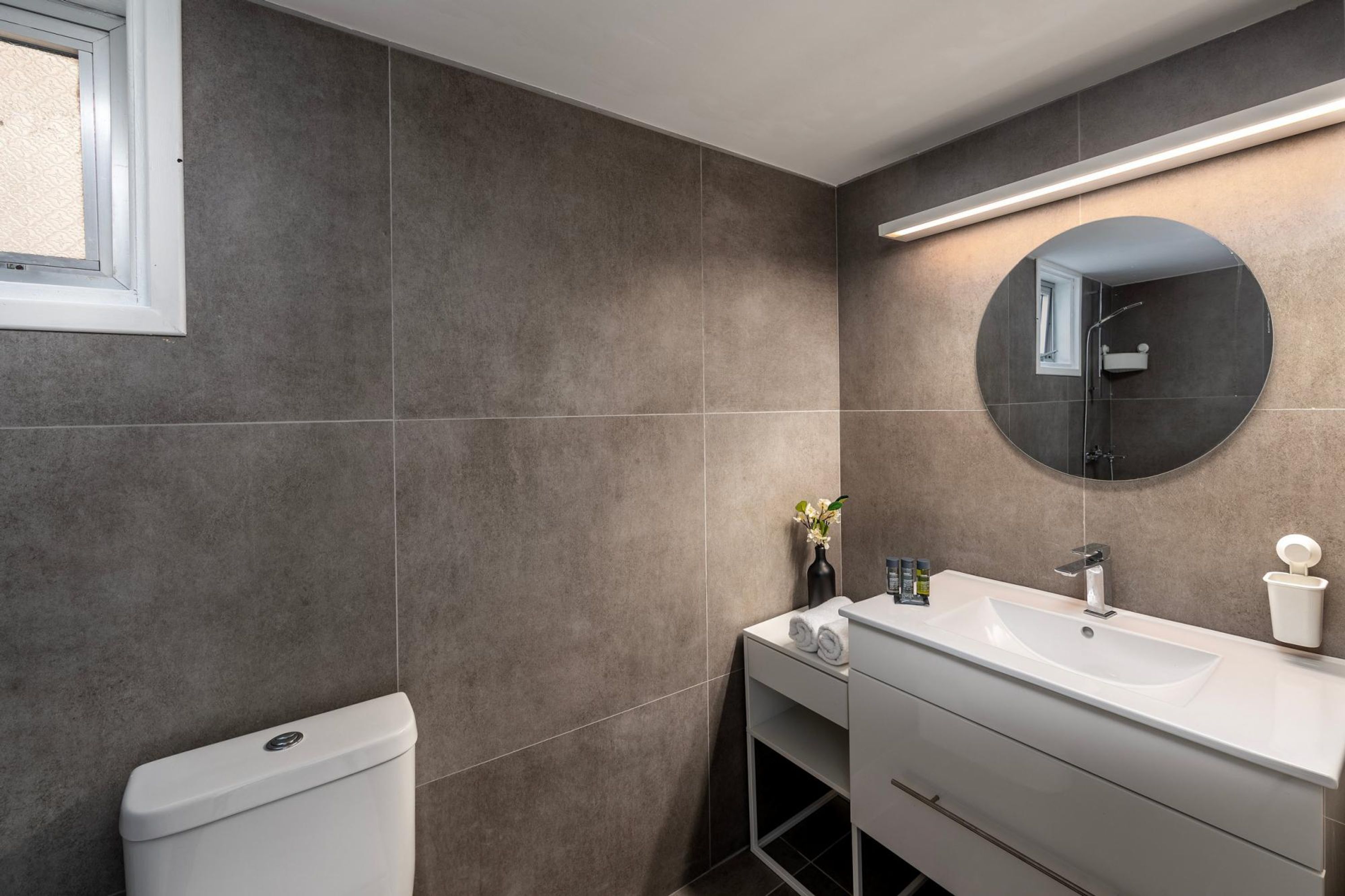 Un baño moderno con un tocador blanco, un espejo redondo y un inodoro.