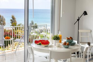 Ein Balkon mit Blick auf das Meer, ein Esstisch mit Speisen und ein weißer Stuhl.