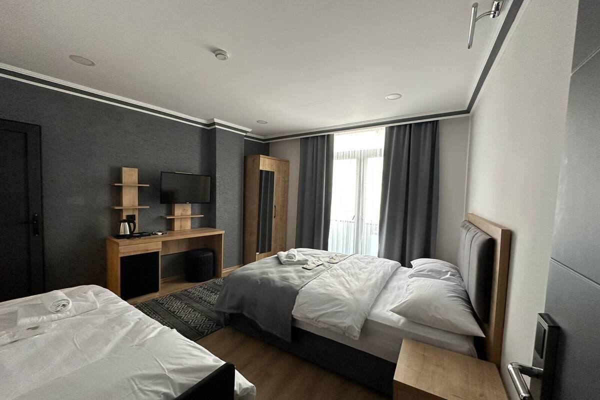 A modern hotel room with a large bed, a desk with a TV, and a wardrobe.