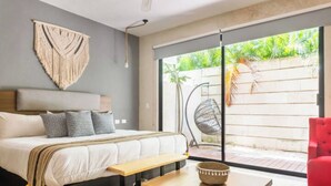 Quarto moderno com cama, um banco de madeira, uma cadeira vermelha e uma janela grande com vista para o verde.