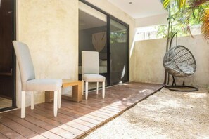 A patio with two chairs and a small table, a hanging chair, and a sliding glass door leading to a room. - Magnificent Apartment Pool Gym (Tulum)