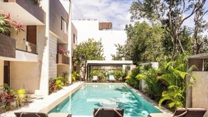 Uma área de piscina moderna com piscina transparente, deck de madeira e espreguiçadeiras.