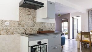 A modern kitchen with a built-in oven, a microwave, and a gas stove. There is a dining area with a table and chairs visible in the background. - Appartement Neuf et son Jardin Pieds Dans le Sable (Saint Paul)
